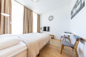 A hotel room with a large bed, a desk, a chair, a TV, and a clock on the wall.