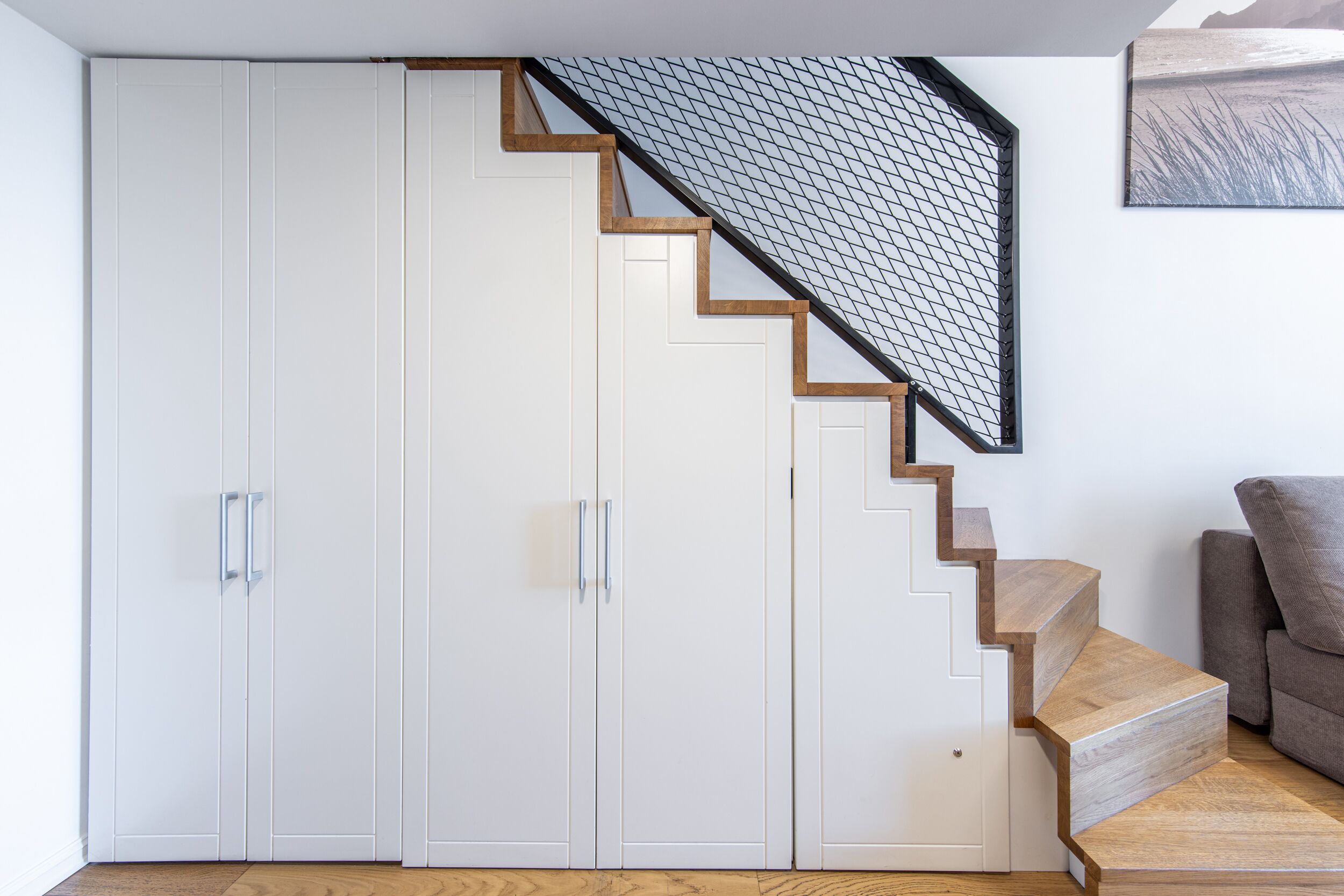 A staircase with wooden steps and a mesh railing, leading to a white wardrobe with silver handles.