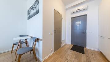 A room with a wooden floor, a white table with two chairs, a grey door, and a wall-mounted air conditioner.