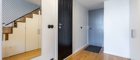 Un pasillo con suelo de madera, una puerta negra y una escalera con paredes color crema y escalones de madera.