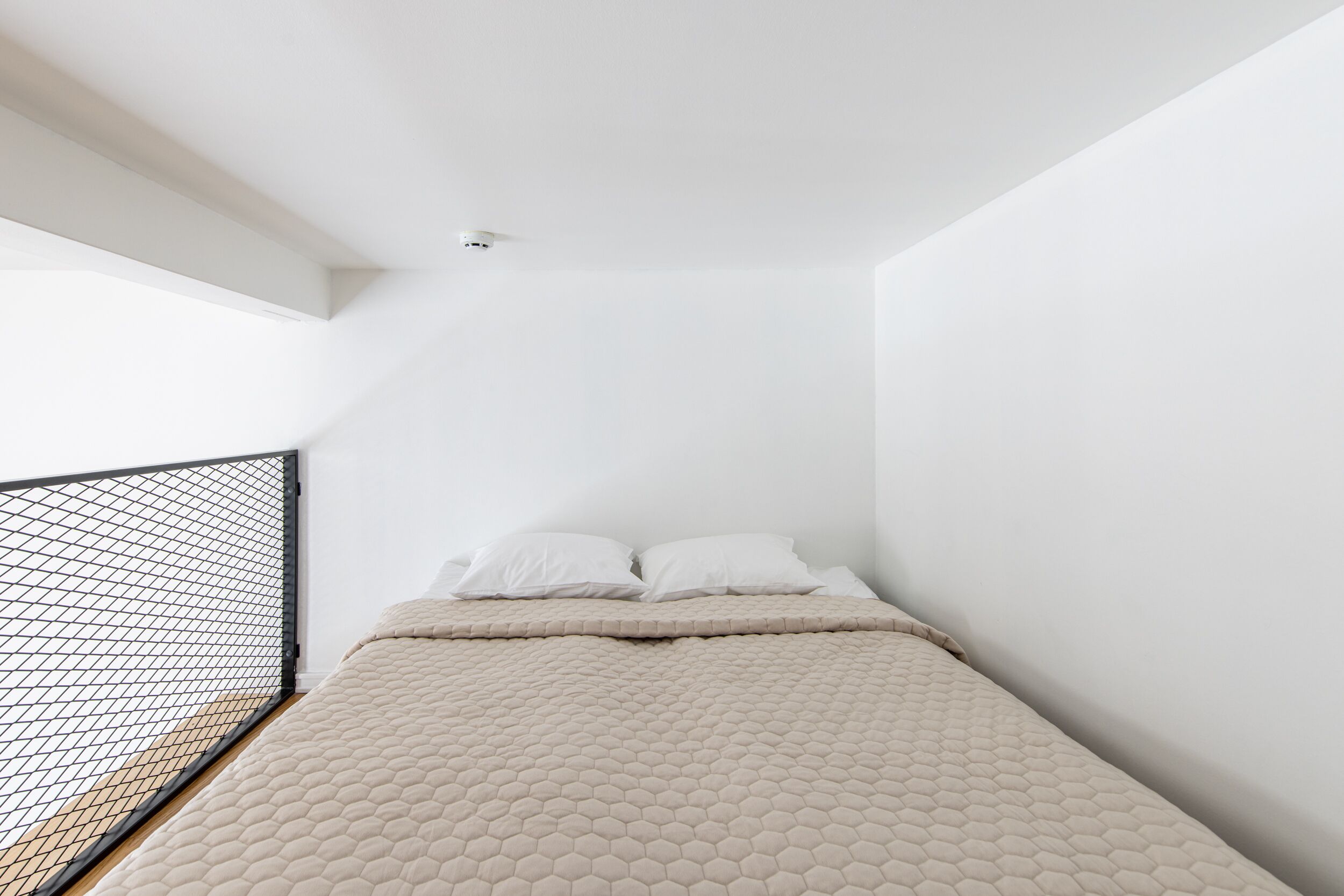 Une chambre à coucher avec un lit, des murs blancs et une rambarde de balcon en treillis noir.