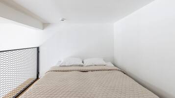 Une chambre à coucher avec un lit, des murs blancs et une rambarde de balcon en treillis noir.