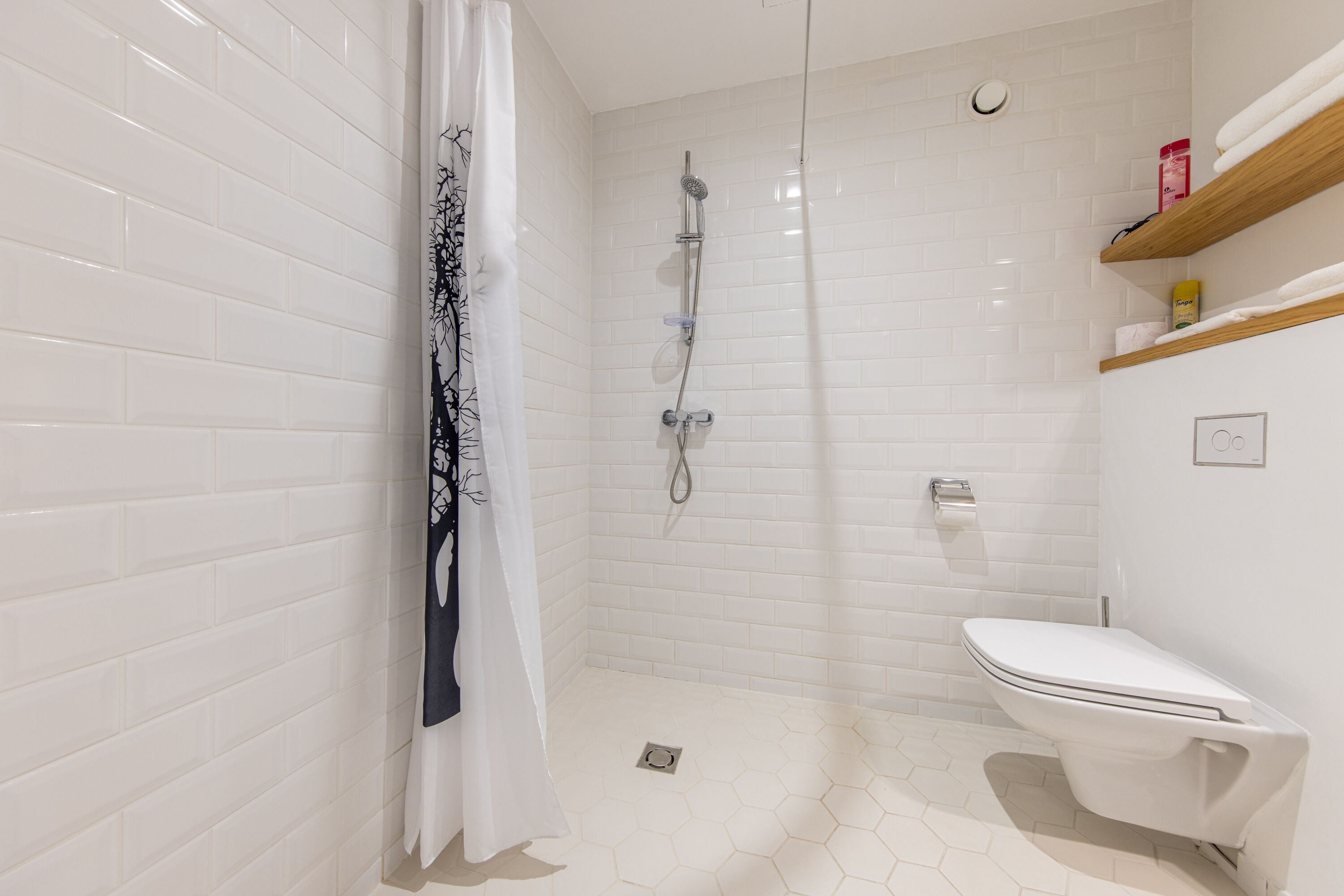 A modern bathroom with white subway tiles, a glass-enclosed shower, a toilet, and a wooden shelf with toiletries.