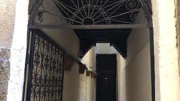 Um corredor estreito com um portão de metal decorativo e uma porta no final.