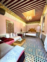 Quarto tradicional com piso xadrez, uma cama com cabeceira, um sofá e uma mesa de centro.