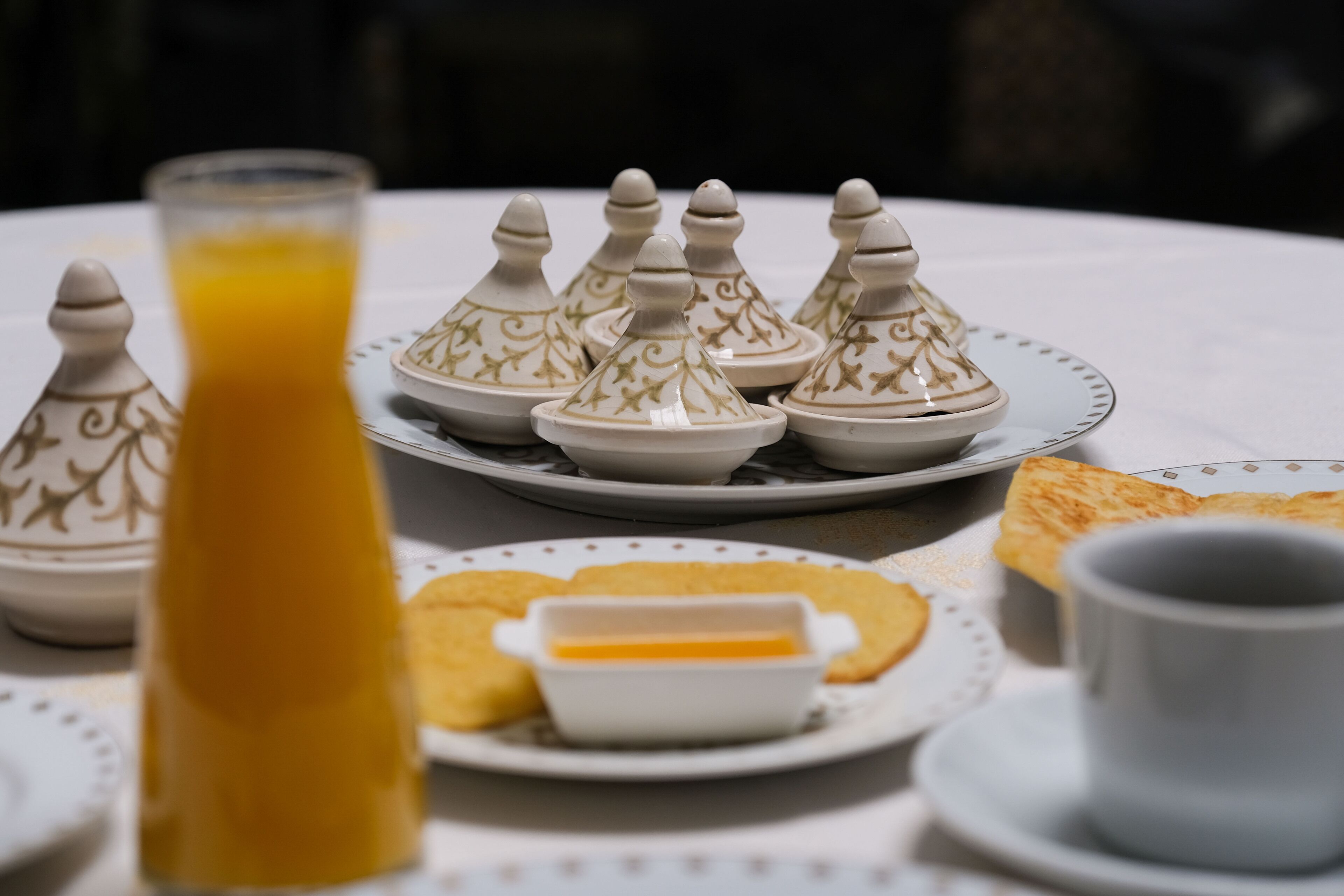 Una mesa dispuesta con teteras de estilo marroquí, un vaso de jugo de naranja y un plato de pasteles.