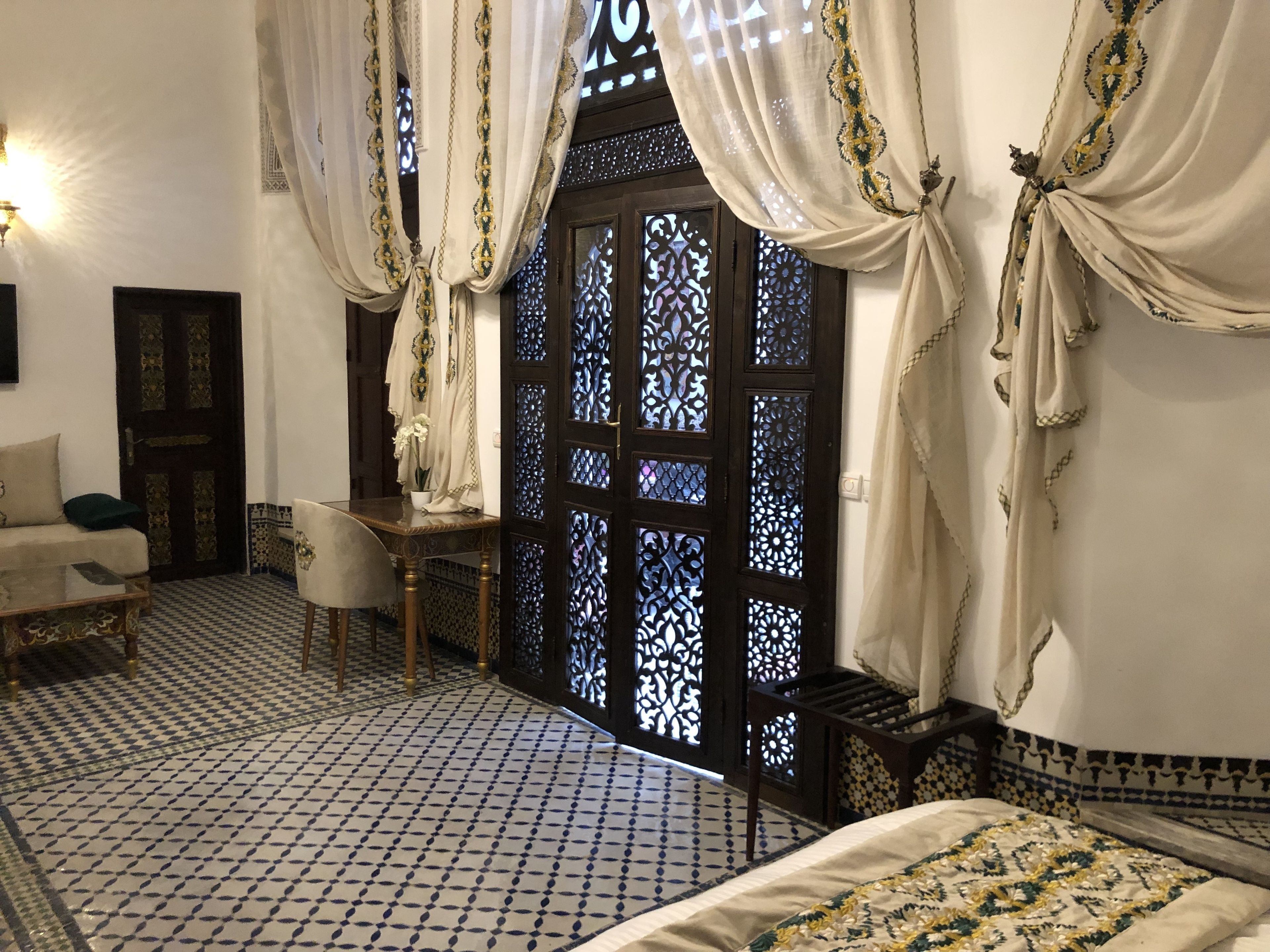 Una habitación con piso a cuadros, un sofá, una mesita y una cama con colcha estampada.