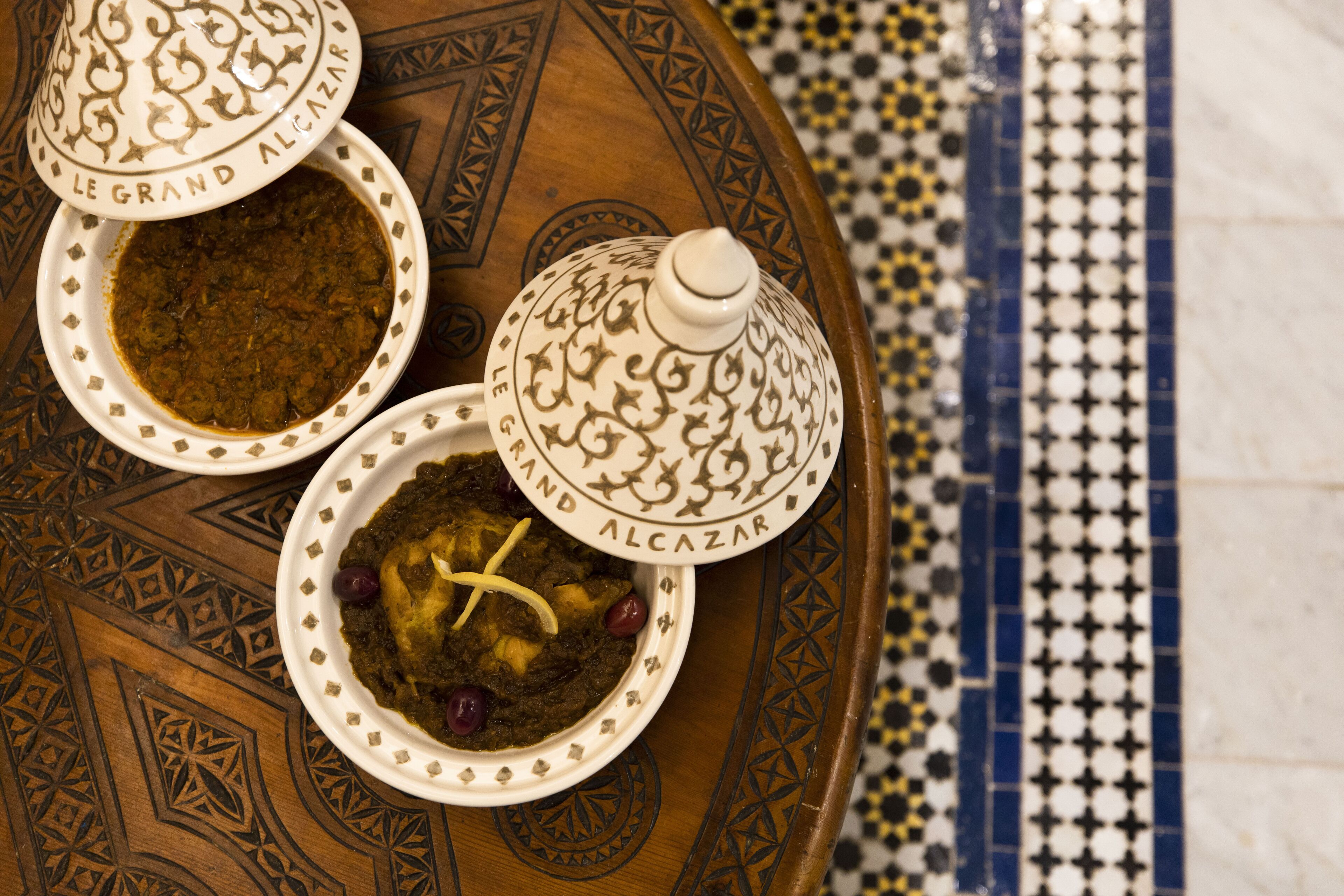 Trois plats en céramique décorés, dotés de couvercles, disposés sur un plateau à motifs.