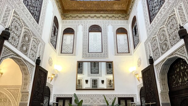 Un área de piscina interior lujosa con detalles de azulejos intrincados, una piscina central y zonas de descanso.