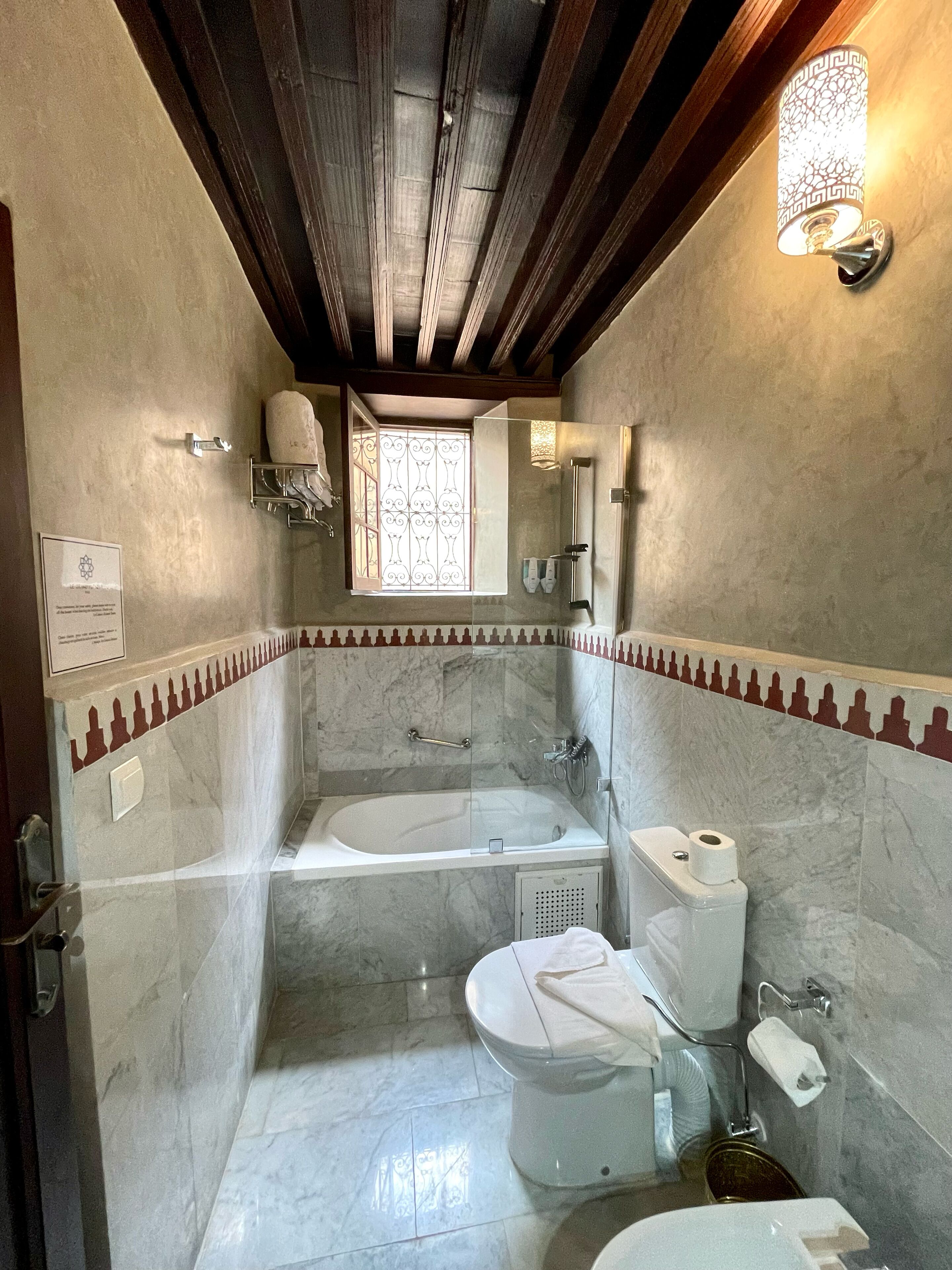 A bathroom with a bathtub, toilet, and sink, featuring marble walls and wooden beams.