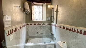 A bathroom with a bathtub, toilet, and sink, featuring marble walls and wooden beams.