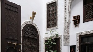 Un interior tradicional marroquí con una gran puerta de madera, un sofá, una mesa con libros y una planta en maceta.