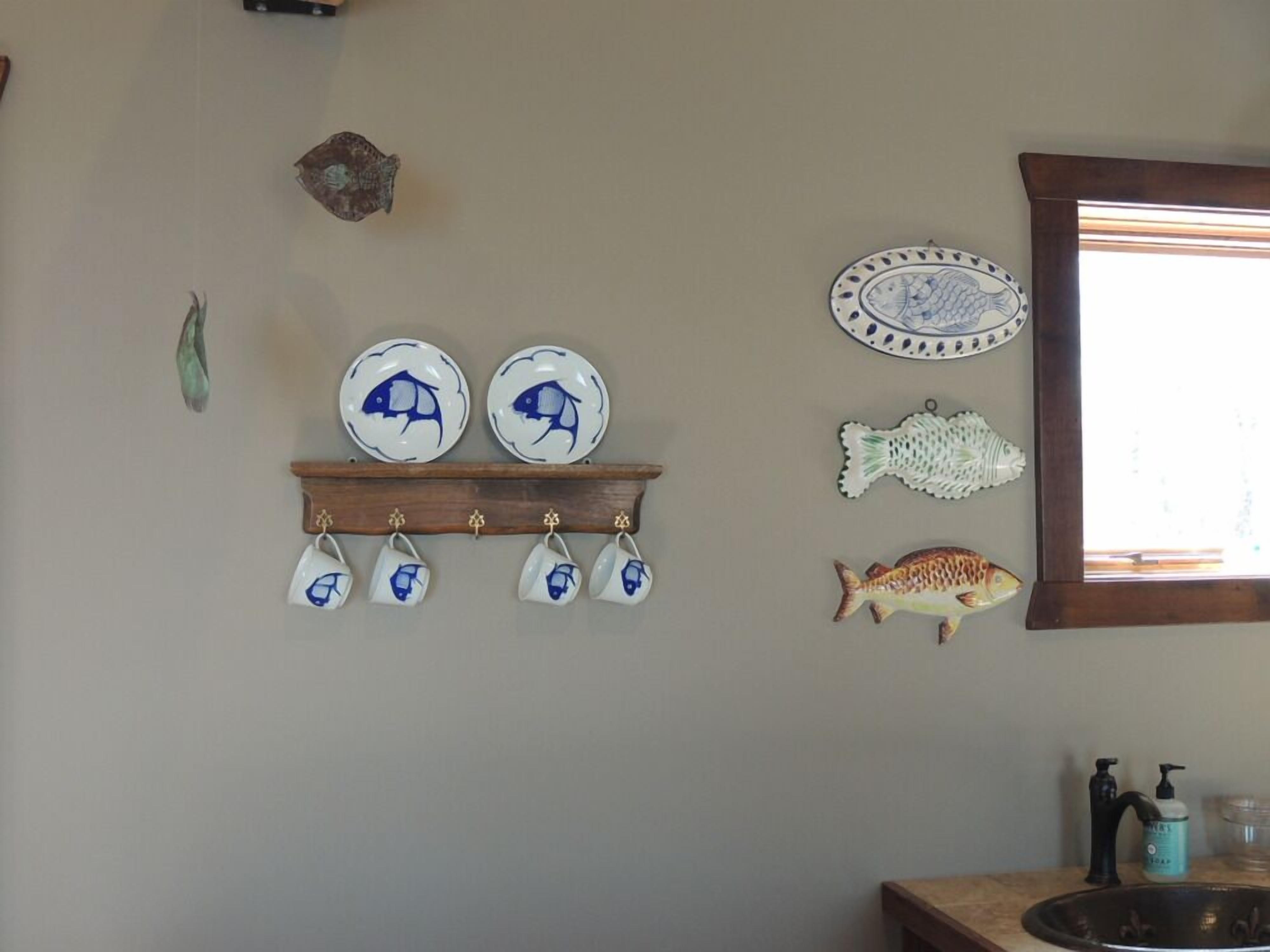 A kitchen with a wooden shelf holding plates and a fish decoration.