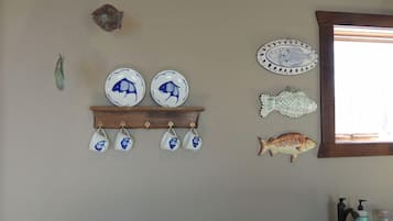 A kitchen with a wooden shelf holding plates and a fish decoration.
