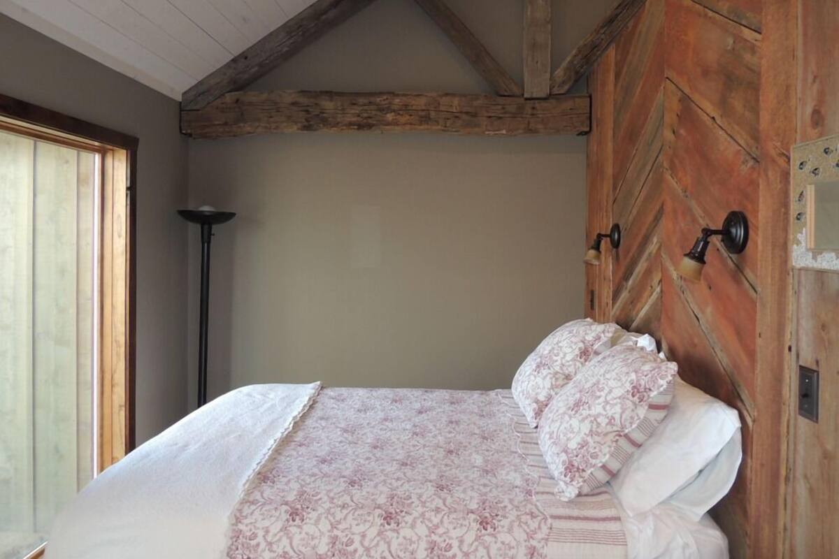 A bedroom with a wooden ceiling, a bed with floral bedding, and a window with blinds.