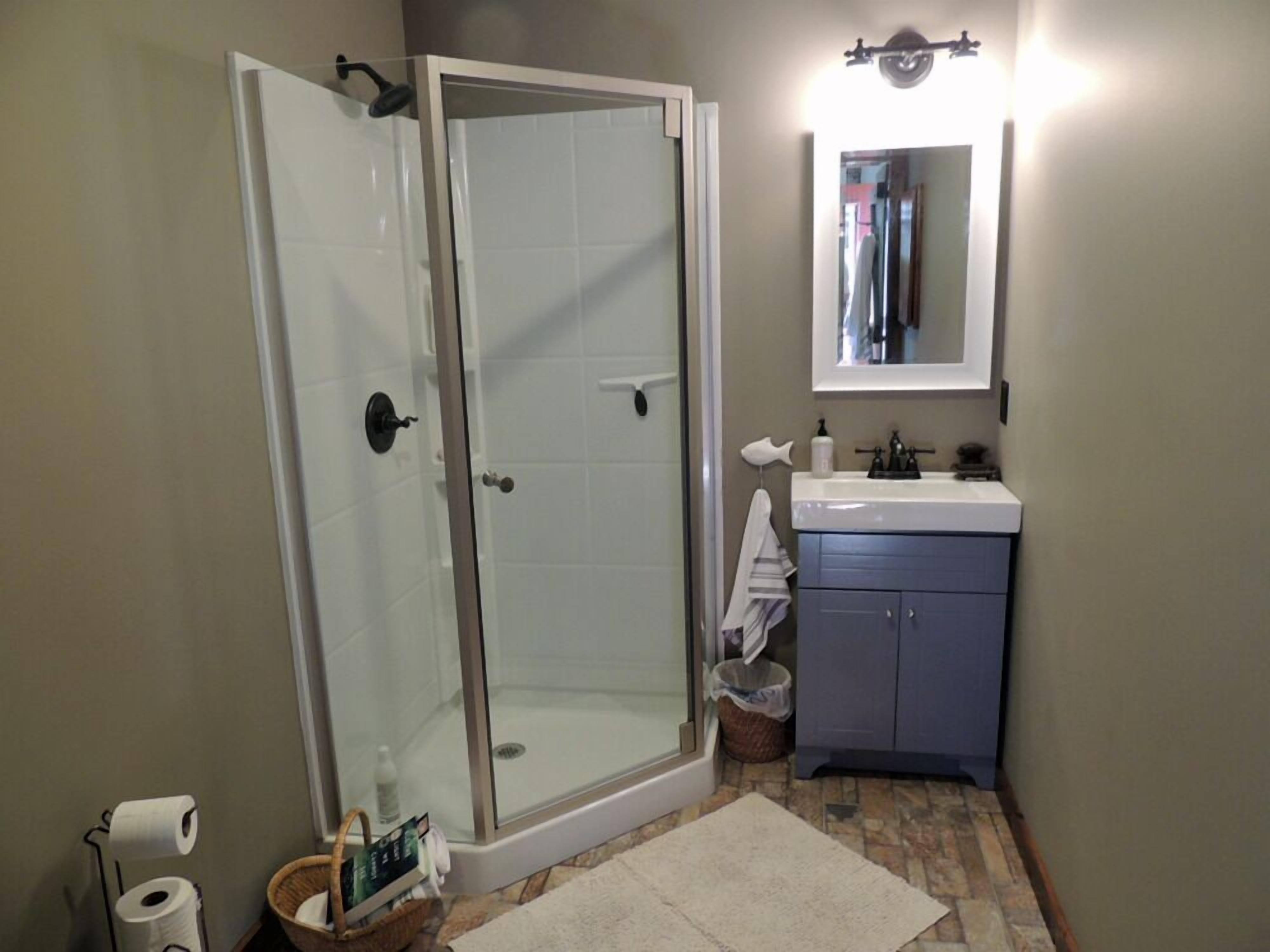 Une salle de bain avec une douche à parois de verre, un lavabo avec un miroir et un sol carrelé.