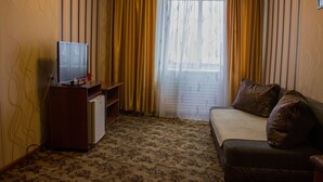 A hotel room with a bed, a television on a wooden cabinet, a small desk, and a window with curtains. - U Svetlany (Cheboksary)