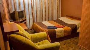 A hotel room with a bed, a chair, a television, and curtains. - U Svetlany (Cheboksary)