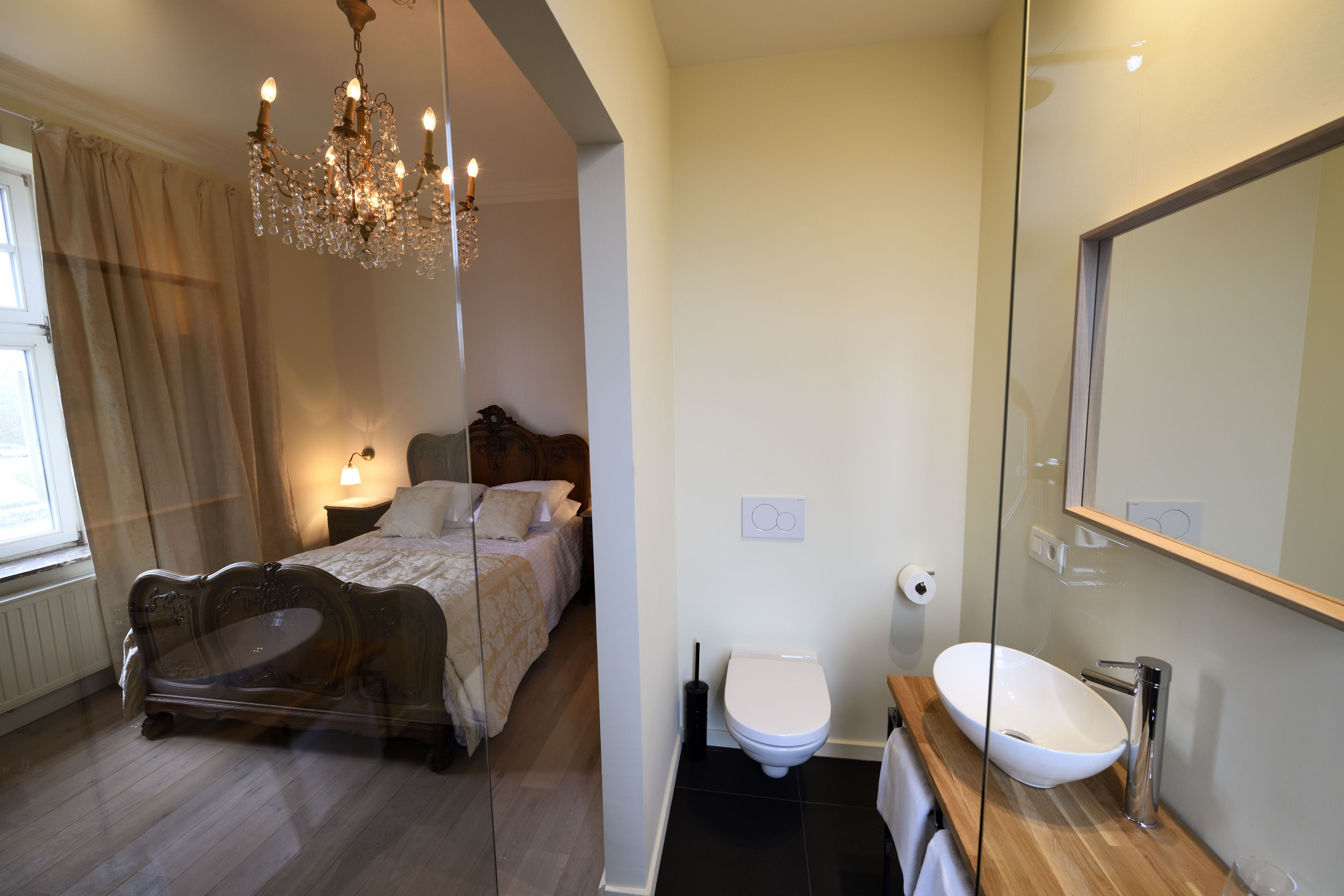 Une chambre à coucher avec un lit, un lustre, une table de chevet et une fenêtre avec des rideaux.