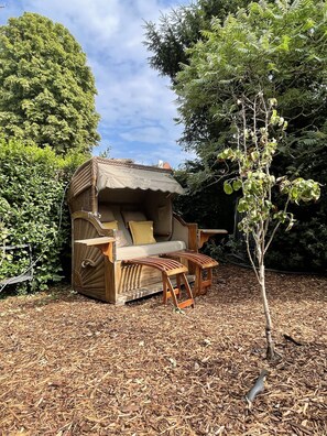 A small, rustic wooden structure with a thatched roof, a cushioned seating area, and a small table.