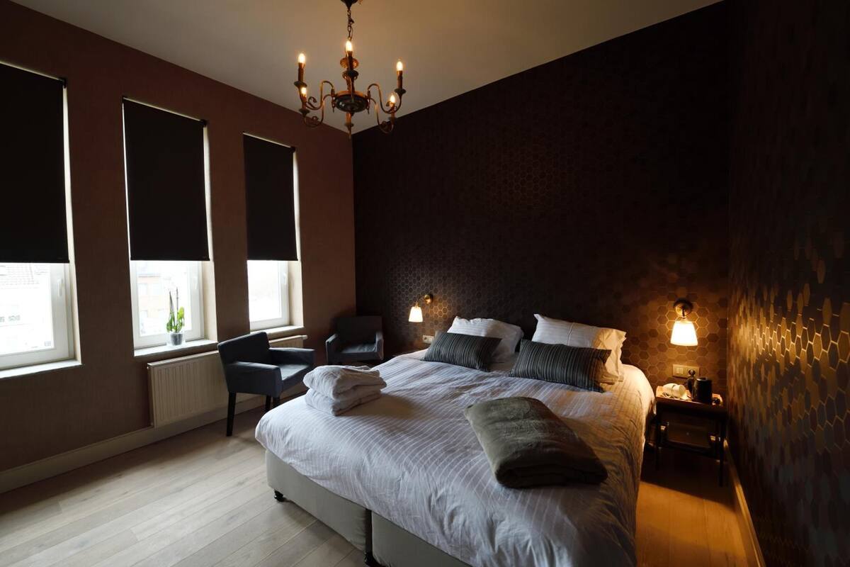 Een slaapkamer met een groot bed, twee bedlampen, een kroonluchter, een stoel en een bureau.