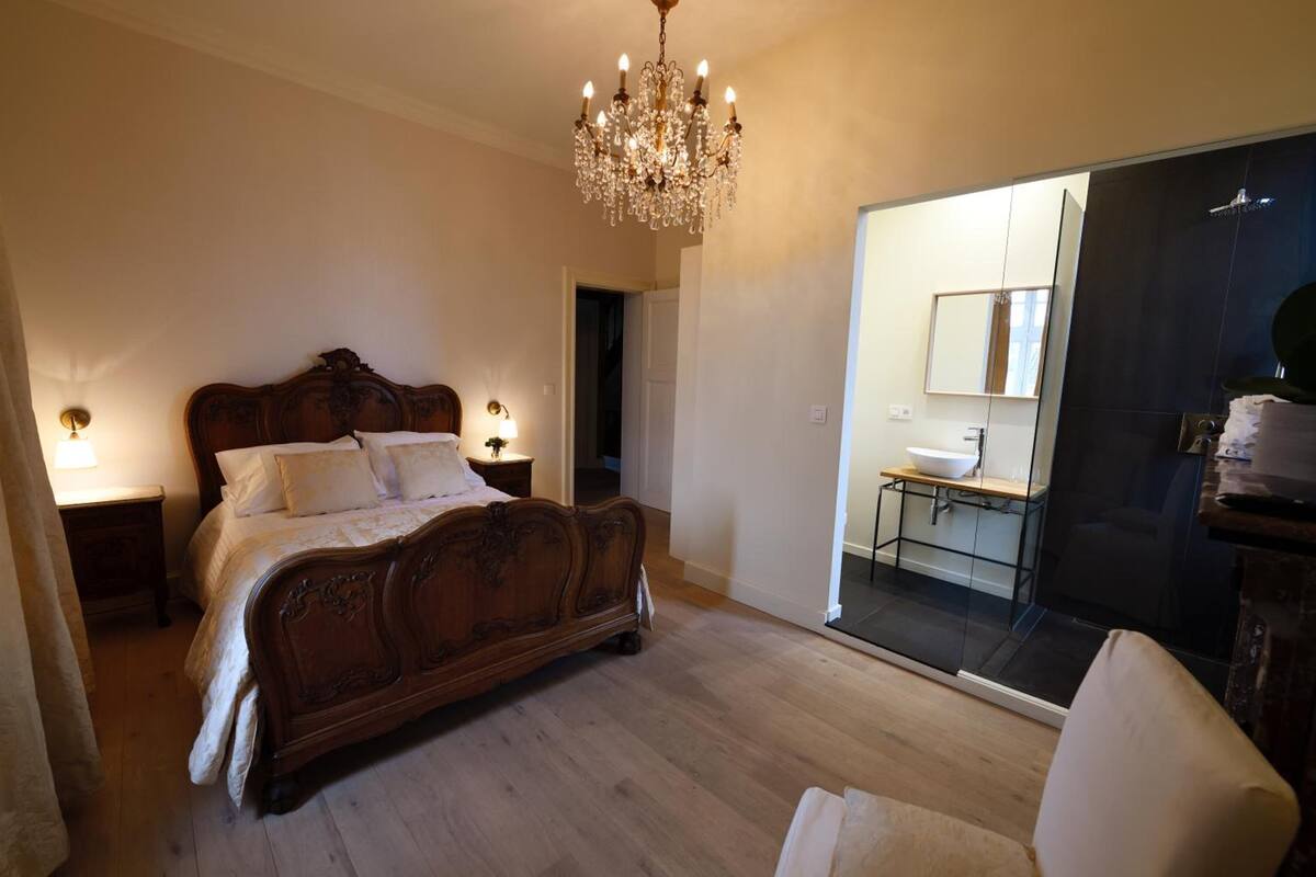 Een slaapkamer met een houten bed, een kroonluchter, een badkamer met een spiegel en een schuifdeur.