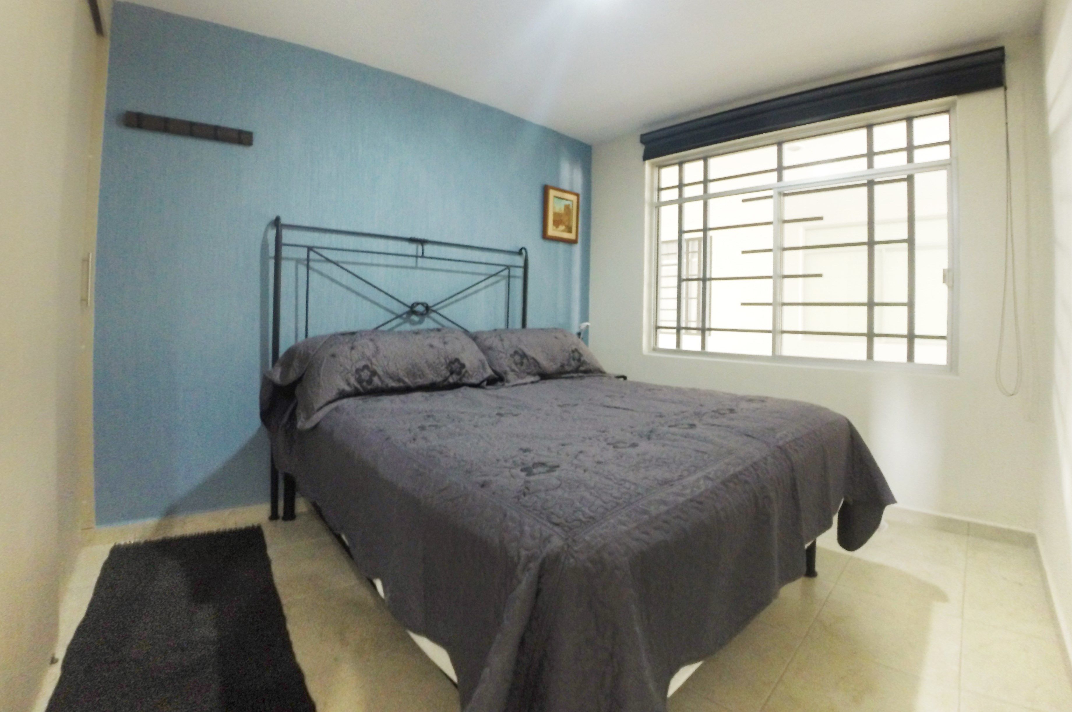 Un dormitorio con una cama, una ventana con barrotes y una pared azul.