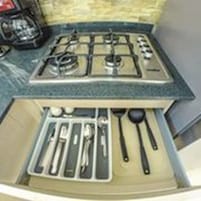 Cocina con estufa a gas, lavamanos y un cajón con utensilios.