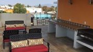 Uma área de estar externa com cadeiras de metal e almofadas vermelhas, uma churrasqueira e vista para o horizonte da cidade.