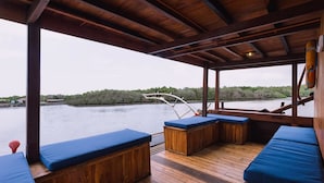 A covered deck with wooden benches and a view of a river. - Situju 7 Cruises (Labuan Bajo)