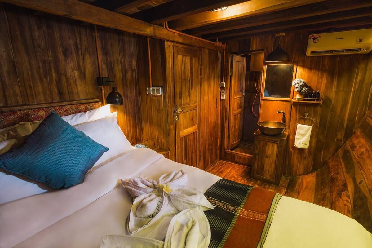 A wooden room with a bed, a bathroom, and a small shelf with toiletries.