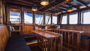 A wooden interior with a bench, tables, and shelves. - Situju 7 Cruises (Labuan Bajo)