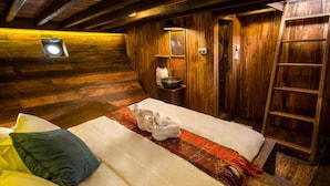 A cozy wooden cabin room with a bed, a small table with a bowl, a ladder, and a wall-mounted light fixture. - Situju 7 Cruises (Labuan Bajo)