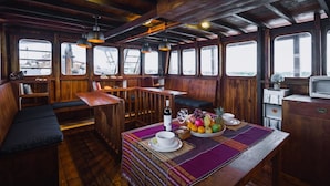 A wooden interior with a bar area, seating, and a table set with fruit and a bottle. - Situju 7 Cruises (Labuan Bajo)