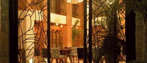 A hotel lobby with a brick wall, a reception desk, and a seating area with chairs and tables.
