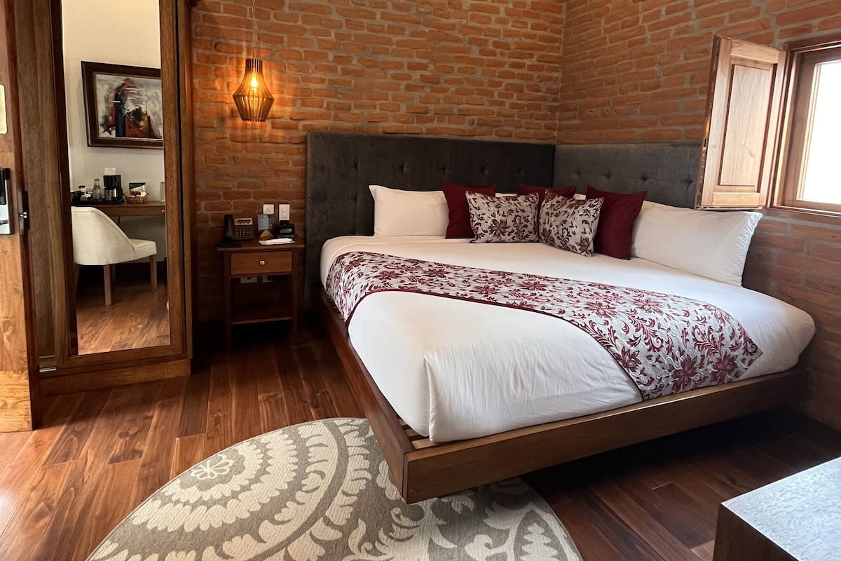 Ein modernes Schlafzimmer mit Backsteinwand, einem großen Bett mit gemusterten Betttextilien, einem Nachttisch, einem Beistelltisch, einem Spiegel und einem runden Teppich.