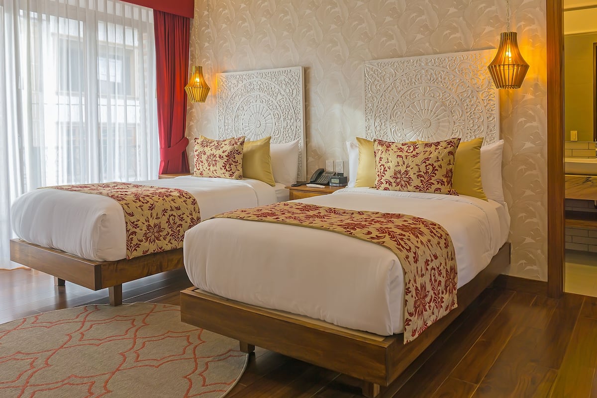 Ein Hotelzimmer mit zwei Betten, Holzboden, einem gemusterten Teppich und einer dekorativen Wandverkleidung.