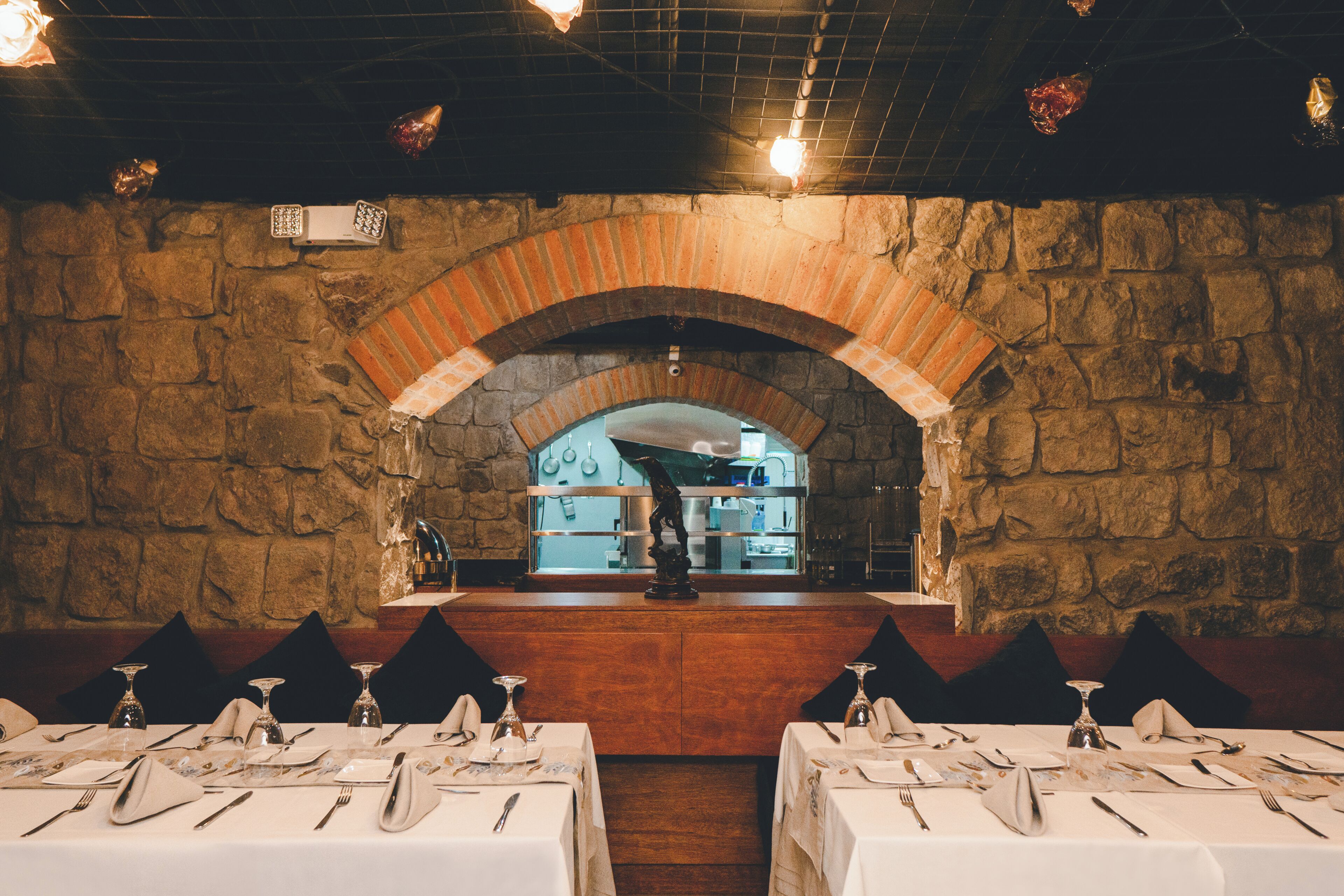 Un interior con paredes de piedra, un arco de ladrillo y mesas dispuestas para comer.