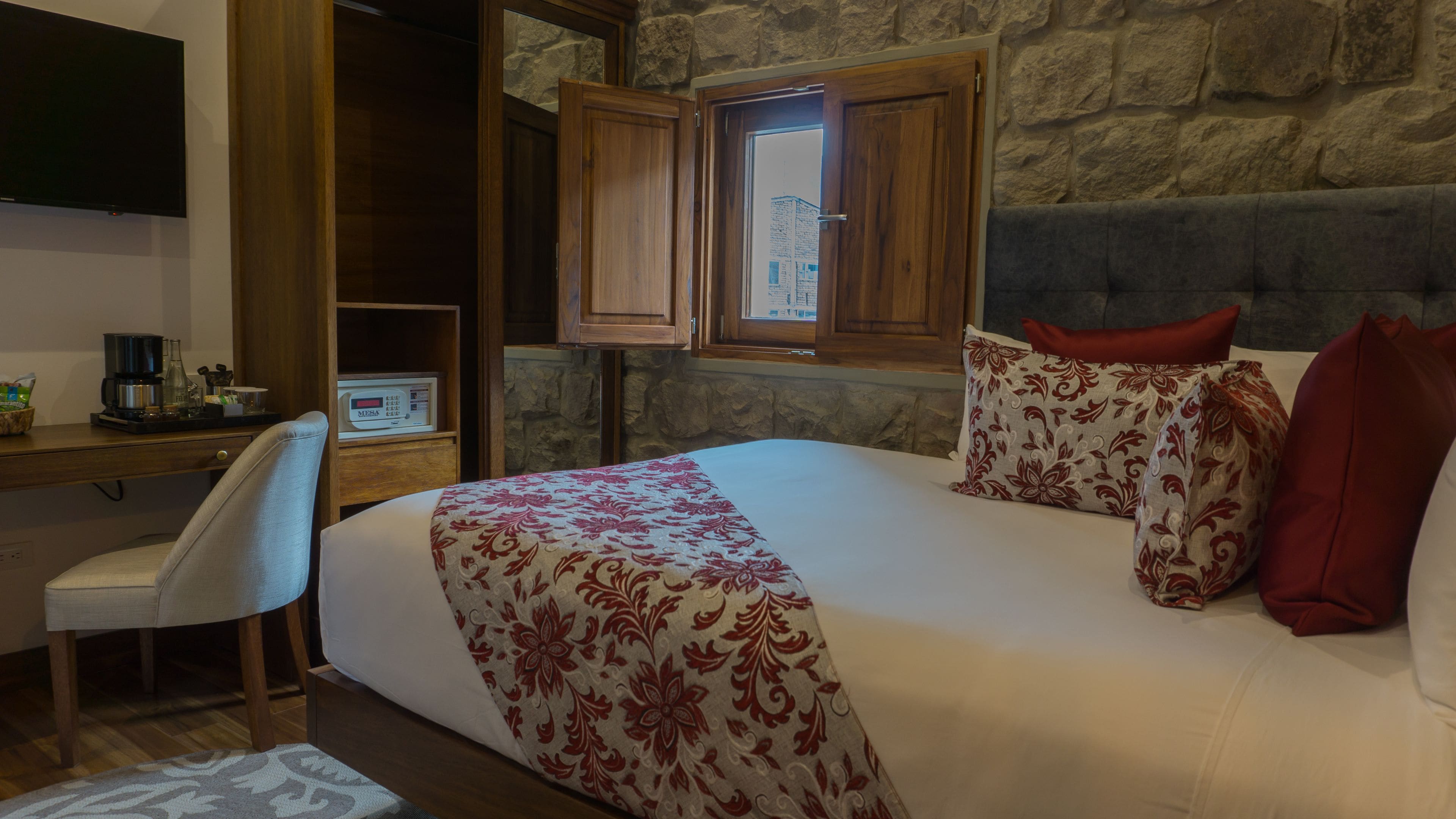 Une chambre d’hôtel avec un lit, un bureau avec un ordinateur, une chaise et un mur en pierre.