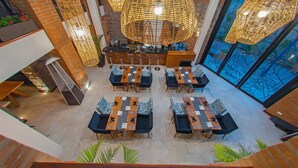 A spacious indoor area with multiple tables and chairs, a reception desk, and large hanging wicker lamps.