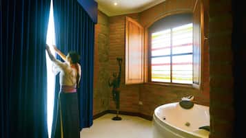A bathroom with a bathtub, a window with blinds, and a statue.