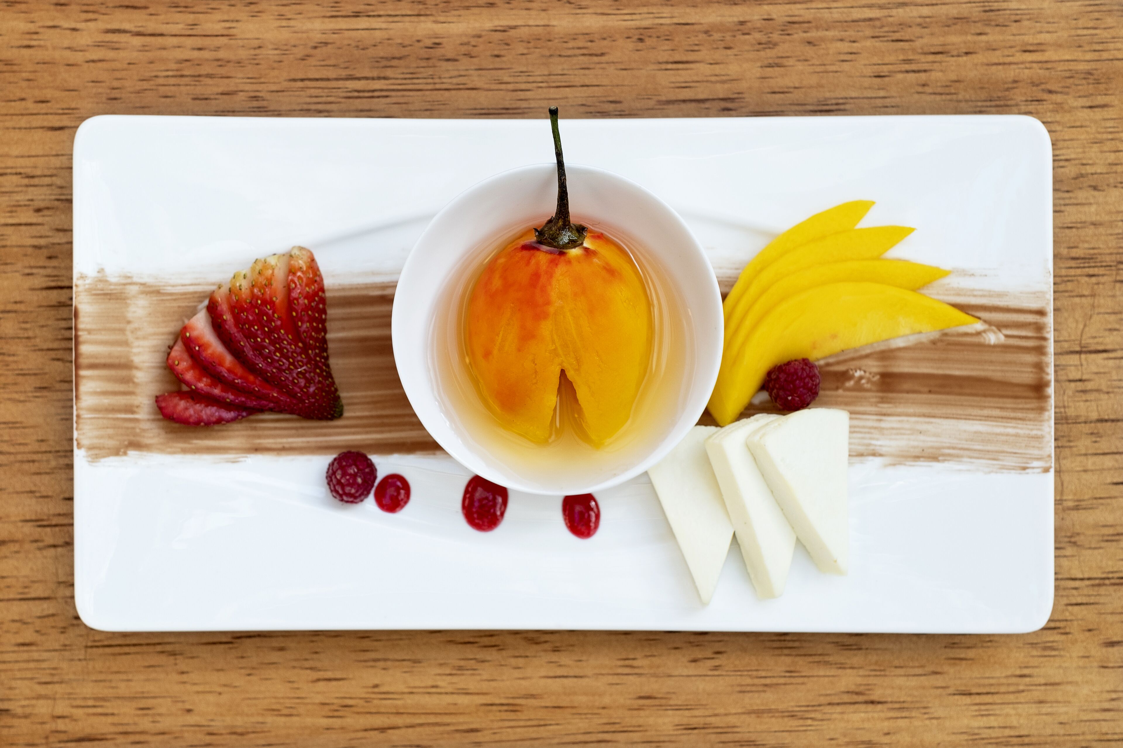 Un plato blanco con un postre que incluye un melocotón, fresas, frambuesas y trozos de mango.