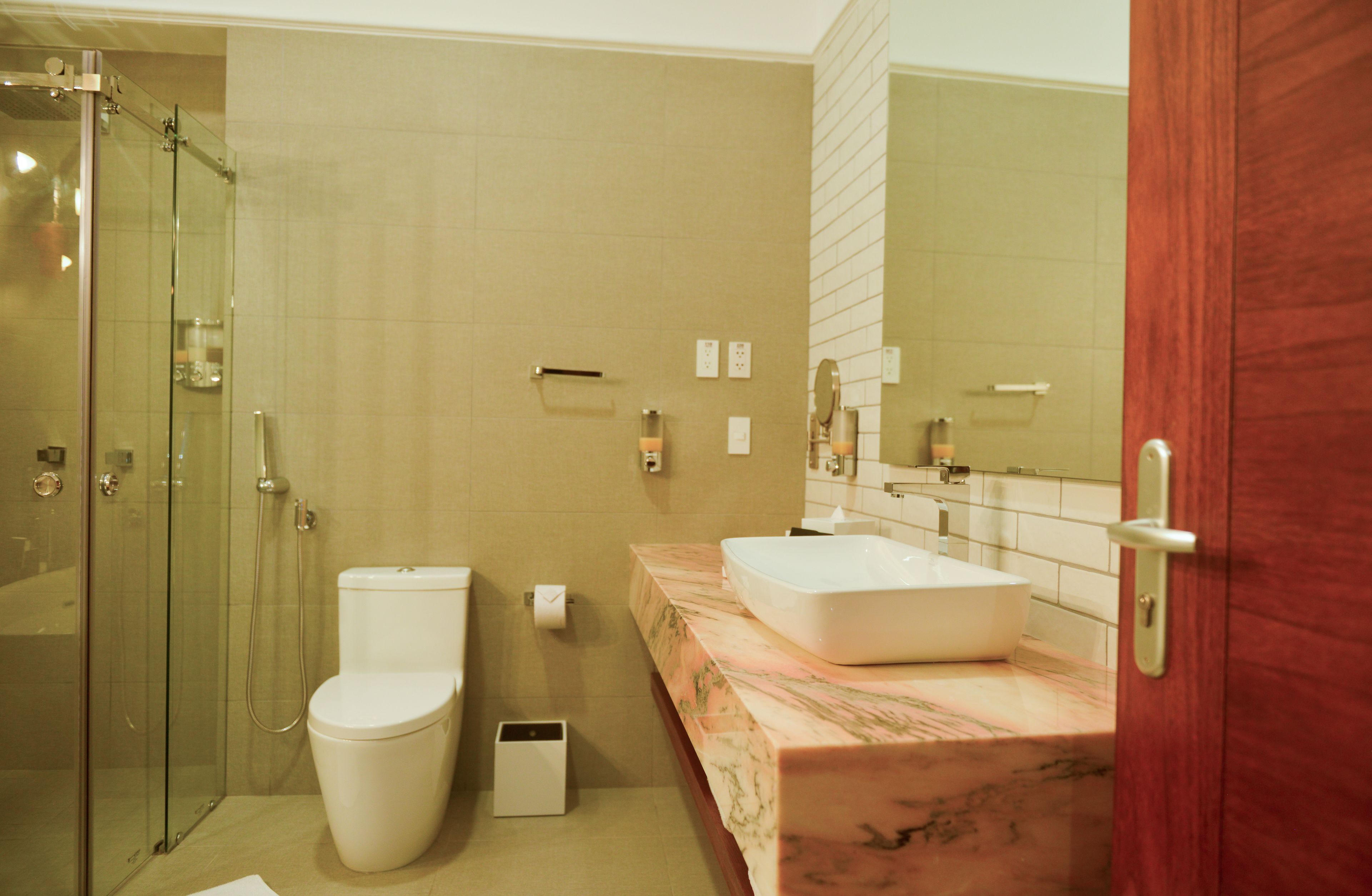 Un baño con ducha envuelta en vidrio, inodoro, lavamanos con encimera de mármol y un espejo grande.