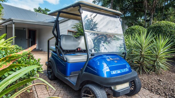 Un carrito de golf estacionado frente a una casa con entrada pavimentada y jardín.