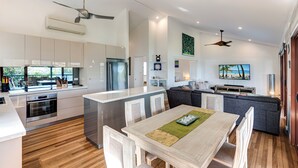 Una cocina moderna con armarios blancos, una isla central y una zona de comedor con mesa y sillas de madera.