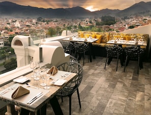 Un restaurante con terraza al aire libre y vistas a un paisaje urbano y montañas.