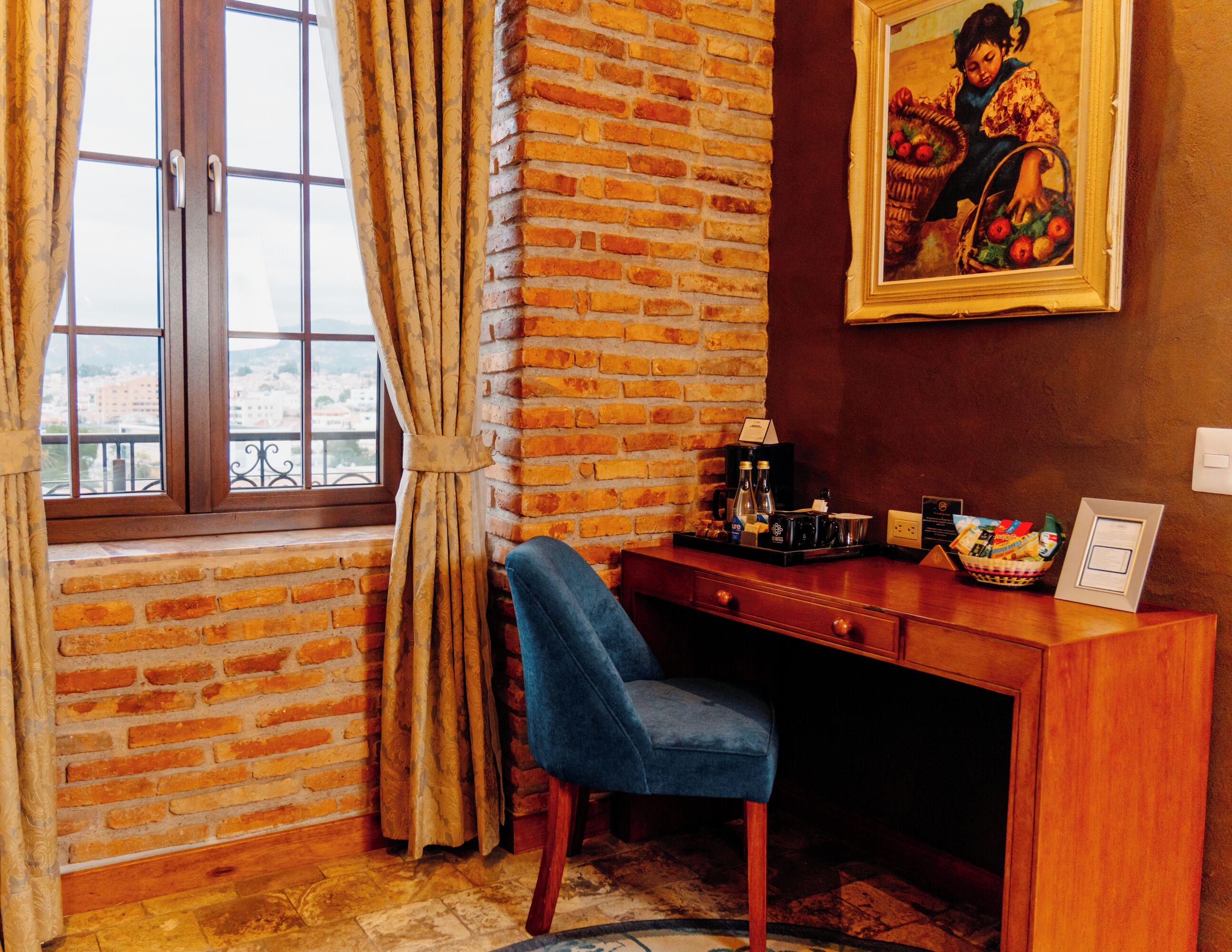Ein Zimmer mit Backsteinwand, Schreibtisch mit Stuhl, Fenster mit Vorhängen und einem Bild an der Wand.