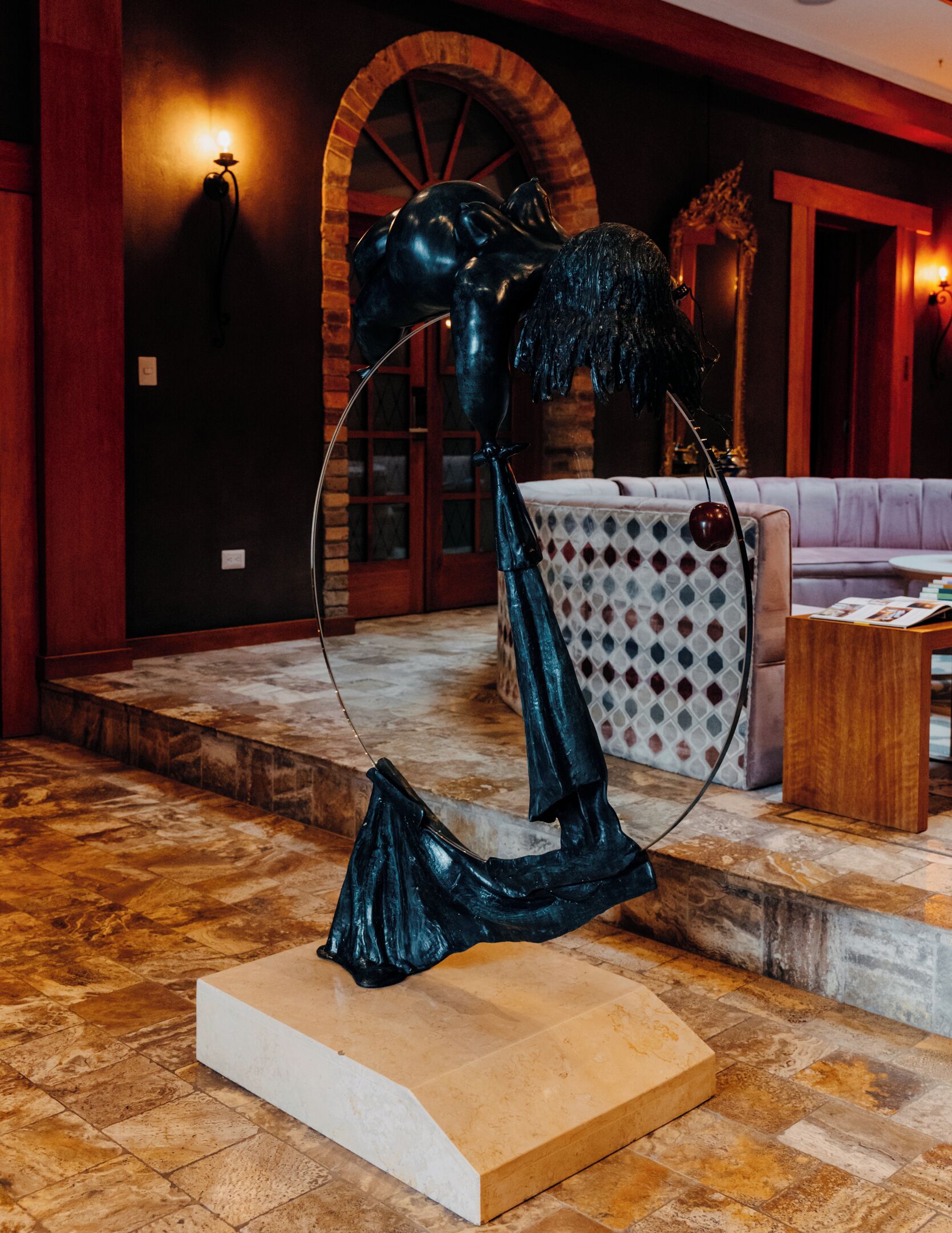 Uma escultura em um saguão com piso de pedra, um sofá estampado e uma mesa de centro de madeira.