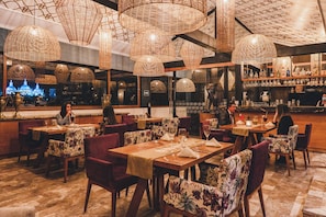 A restaurant with tables set for dining, wicker ceiling lamps, and a bar area with shelves of bottles. - Hotel Cruz del Vado by Art Hotels Ecuador (Cuenca)