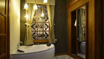 Un baño con una bañera independiente, un ventanal con cortinas decorativas y un armario espejo.